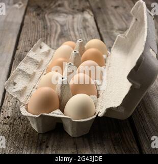 Uova intere fresche in confezione di carta su fondo grigio di legno, primo piano Foto Stock