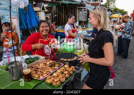 Giovane donna bionda ride insieme ad una venditore che vende pancake di cocco in una bancarella lungo Sisavangvong Road (la strada principale), Luang Prabang, Lua Foto Stock