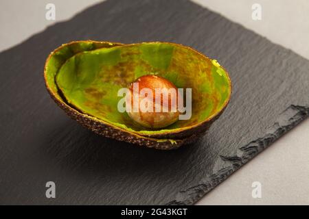 Resti dell'Aavocado mangiato - buccia e semina sopra superficie di pietra scura Foto Stock