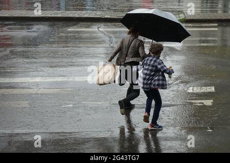 Bucarest, Romania - 18 giugno 2021: La gente attraversa la strada sulla strada in Piazza Unirii, durante la pioggia battente, a Bucarest, Romania. Questa immagine è per e. Foto Stock