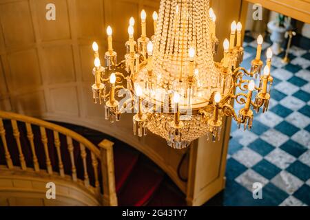 Vista dall'alto di un antico lampadario. Un enorme lampadario in oro di cristallo con candele, sullo sfondo di una scala a chiocciola e un Foto Stock