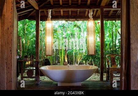 Vasca indipendente all'interno di un bagno aperto in una vecchia casa di legno a Bali. Bali, Indonesia. Foto Stock