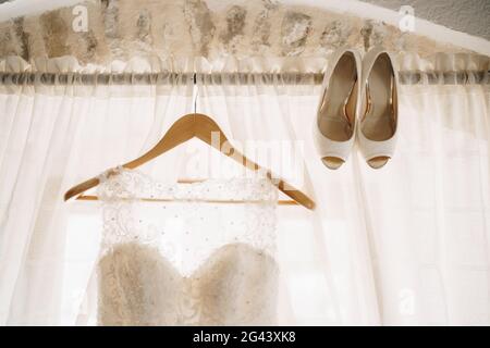 Appendiabiti in legno con l'abito della sposa sul cornicione e le scarpe da sposa. Foto Stock