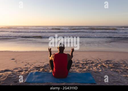 Vista posteriore dell'uomo afro-americano anziano meditando e praticando yoga mentre si siede sul tappetino yoga a. Foto Stock