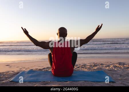 Vista posteriore dell'uomo afro-americano anziano con le braccia larghe aperto praticando yoga in spiaggia Foto Stock