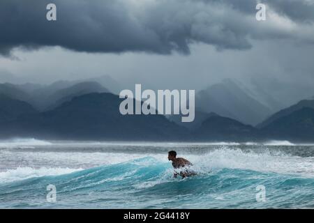 Surfer on wave in Teahupoo surf area con tempeste nuvole e montagne dietro, Tahiti Iti, Tahiti, Windward Islands, Polinesia francese, Sud Pacifico Foto Stock