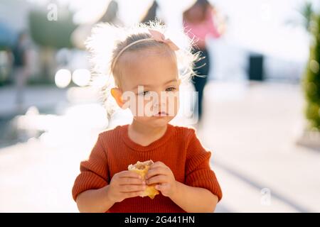 Carino bambina sta mangiando una torta vicino alla fontana nel parco Foto Stock