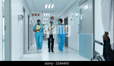 Gruppo vario di medici maschili e femminili che indossano maschere facciali camminare guardando il tablet Foto Stock