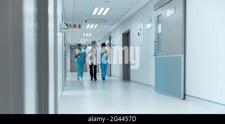 Gruppo vario di medici maschili e femminili che indossano maschere facciali camminare guardando il tablet Foto Stock