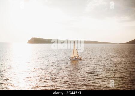 La barca a vela bianca naviga sul mare sullo sfondo della montagna. Il sole splende di luce Foto Stock