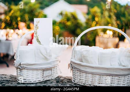 Cartoncino bianco con supporti ornamentali su asciugamano laminato in cesto di vimini bianco sul tavolo. Grandangolo Foto Stock