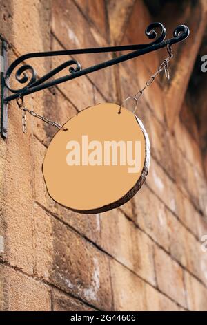 Cartello rotondo in legno vuoto appeso su catene su un forgiato pin su un antico muro di pietra Foto Stock