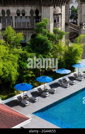 Piscina con ombrelloni blu, situata contro un vecchio edificio e lussureggiante vegetazione. Kuala Lumpur, Malesia. Foto Stock