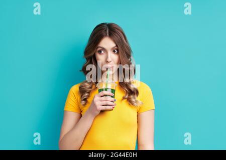 Bella donna bere gustoso succo di detox verde su sfondo blu Foto Stock