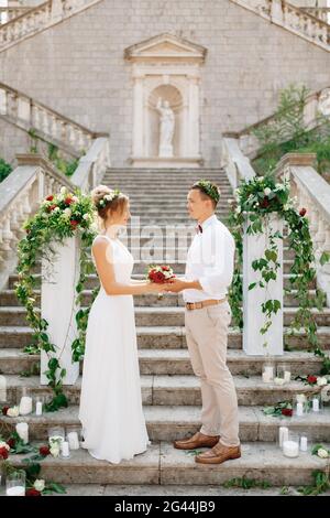 La sposa e lo sposo si trovano sulle scale della Natività della chiesa della Beata Vergine Maria a Prcanj e tengono un bouque di nozze Foto Stock