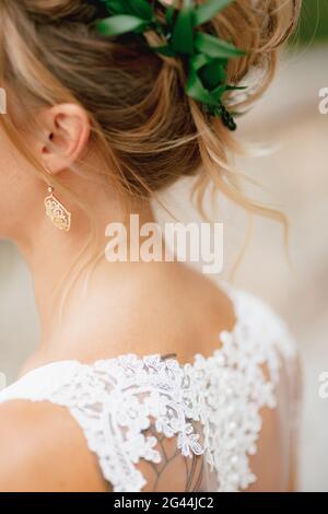 Sposa bionda in un abito in pizzo con un grazioso orecchino in orecchio e una corona di olive, primo piano Foto Stock