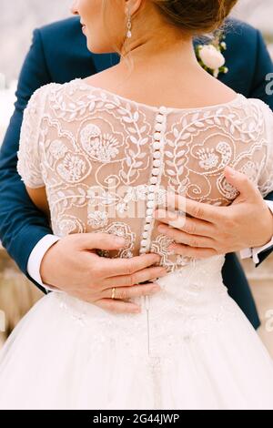 La sposa e lo sposo sono in piedi e abbracciano, mani dello sposo sulla schiena della sposa, primo piano Foto Stock