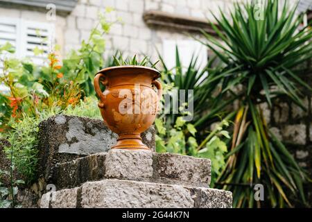 Primo piano di un vaso di fiori di strada sui gradini sullo sfondo di un muro di mattoni e verde nel cortile. Foto Stock