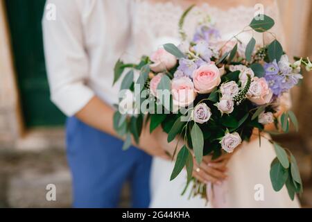 La sposa e lo sposo stanno abbracciando e tenendo un bouquet di nozze di rose, delfinio e rami di eucalipto nelle loro mani, cl Foto Stock