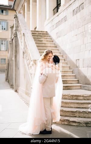 Groom tiene la sposa tra le sue braccia vicino ai gradini di un vecchio edificio a Bergamo, Italia Foto Stock