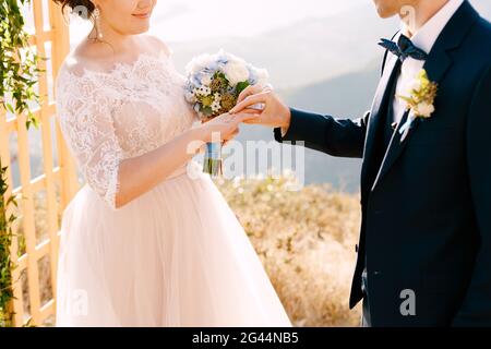 Lo sposo mette l'anello di nozze sul dito della sposa. Sta sorridendo Foto Stock