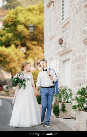 La sposa e lo sposo camminano tenendo le mani vicino a uno splendido Casa in mattoni nella città vecchia di Perast Foto Stock