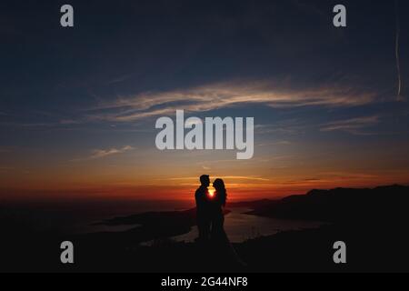 Silhouette della sposa e dello sposo che stanno abbracciando sopra Monte Lovcen con vista sulla Baia di Cattaro al tramonto Foto Stock