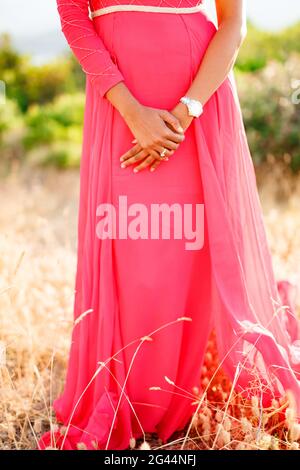 Una donna in un elegante abito rosa caldo con un la gonna lunga si erge tra gli spikelets con le mani piegate Foto Stock