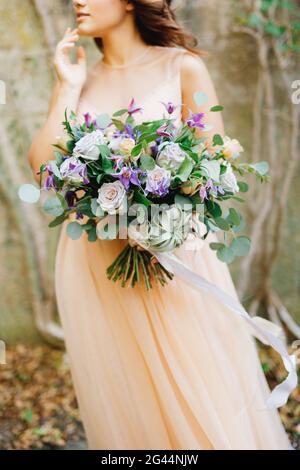 Mezzo-ritratto di una sposa in un abito beige e un bel bouquet di rose in mano Foto Stock