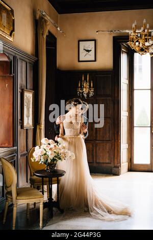 Sposo abbracci sposa da dietro vicino al tavolo con un bouquet di rose in una vecchia villa. Lago di Como Foto Stock