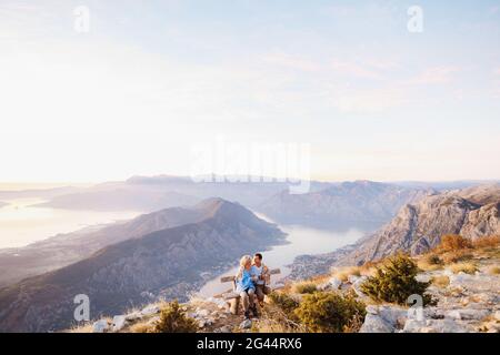 Abbracciando coperto con una coppia coperta siede su una panchina e beve il tè sullo sfondo di un panorama montano Foto Stock