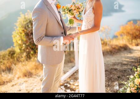 La sposa e lo sposo stanno in piedi sul Monte Lovcen vicino l'arco di nozze e le mani di tenuta Foto Stock