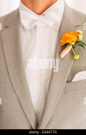 Lo sposo in un abito grigio con una cravatta di prua bianca e una boutonniere con fiori d'arancio in una camera d'albergo, primo piano Foto Stock