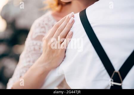 Sposa in pizzo bianco abito mettere la sua mano sulla spalla dello sposo in camicia bianca. Primo piano Foto Stock