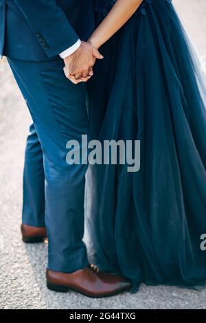 Lo sposo in una tuta blu tiene la mano della sposa in un abito blu. Primo piano. Vista dal basso Foto Stock
