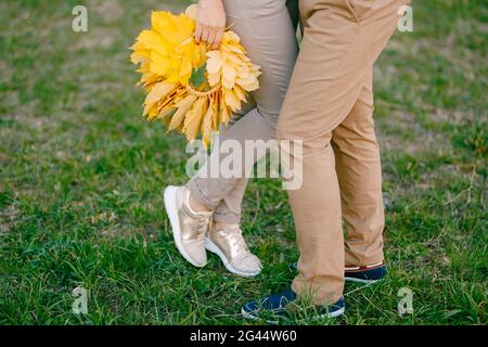 La donna sta in piedi sulla punta accanto all'uomo, tenendo in mano una corona di foglie gialle. Le gambe si avvicinano Foto Stock