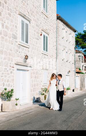 La sposa e lo sposo si abbracciano lungo il Strade di Perast vicino a case di mattoni bianchi Foto Stock