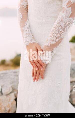 La sposa in abito con maniche in pizzo ha piegato le mani con un anello di nozze sul suo dito, primo piano Foto Stock