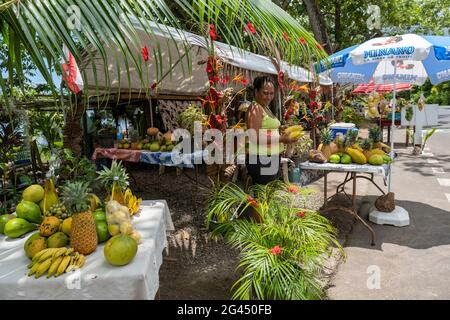 La donna vende frutta tropicale in uno stand di frutta e verdura a bordo strada a Papetoai, Moorea, Windward Islands, Polinesia francese, Sud Pacifico Foto Stock