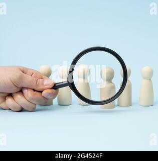 Figure di uomini in legno si trovano su uno sfondo blu e una lente d'ingrandimento nera Foto Stock