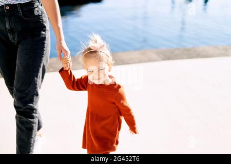 Carino ragazza di 2 anni sta tenendo la mano della madre durante una passeggiata sul mare Foto Stock