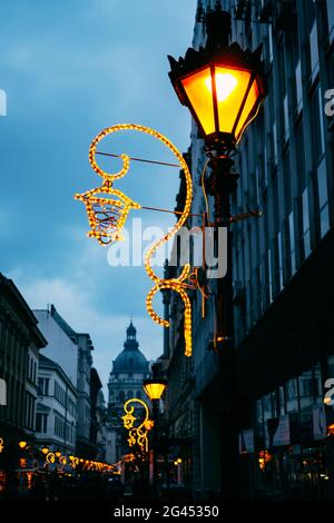 Una lampada da strada illuminata di notte con illuminazione a LED di fronte a un edificio a più piani lungo una lunga strada. Foto Stock
