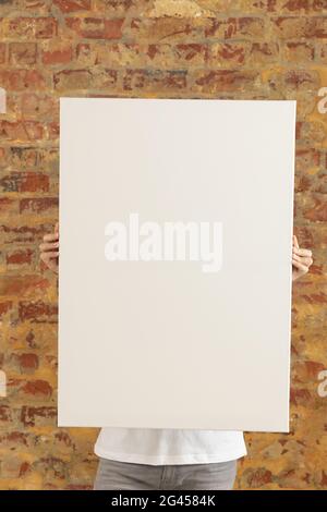 Tela vuota tenuto di fronte a un muro di mattoni Foto Stock
