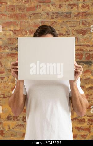 Tela vuota tenuto di fronte a un muro di mattoni Foto Stock
