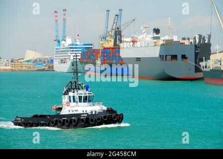 Una varietà di navi ormeggiate nelle acque turchesi del porto autonomo di Cotonou, Benin, Africa occidentale, mentre un rimorchiatore viaggia in primo piano. Foto Stock