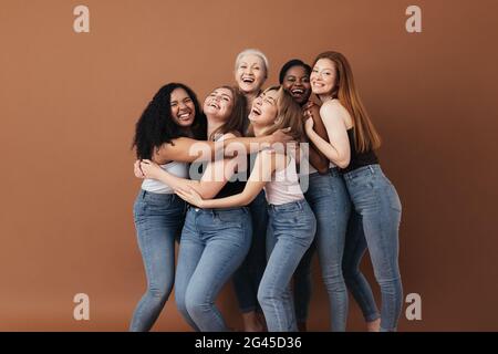 Sei donne ridenti di razza, età e tipo di figura diversi. Gruppo di femmine multirazziali che si divertono su uno sfondo marrone. Foto Stock