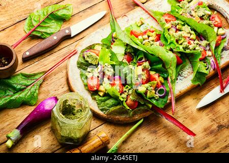 Insalata di vitamina estiva in cucina board.Salad con pomodoro, avocado, salsa di pesto in foglie di bietole. Foto Stock