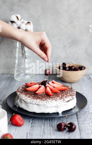 Dolce torta di frutti di bosco decorata con ciliegie e fragole, ricoperta di panna bianca. Dolce cibo ancora vita. Foto Stock