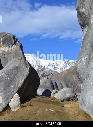 Vista attraverso i massi di granito a Kura Tawhiti o Castle Hill Conservation Site sull'Isola del Sud della Nuova Zelanda con montagne innevate Foto Stock