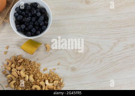 Vista di una varietà di noci e muesli, ciotole di frutta secca e uova su superficie di legno Foto Stock